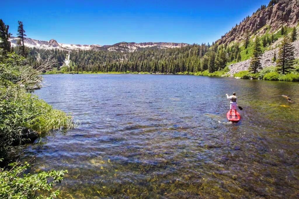 Ein klarer See mit einem Kanu im Vordergrund und einem bewaldeten Berg im Hintergrund.