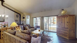 A spacious living room with leather sofas, a wooden coffee table, a chandelier, and a large wooden cabinet. - Townhome-Style Property with Private Hot Tub and Gorgeous Forest Views (Mammoth Lakes)