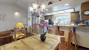 A dining area with a wooden table, chairs, a chandelier, and a vase with flowers. - Townhome-Style Property with Private Hot Tub and Gorgeous Forest Views (Mammoth Lakes)