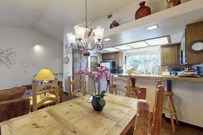 Ein Essbereich mit Holztisch, Stühlen, einer Kristallleuchtre und einer Blumenvase.