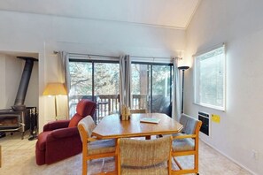A room with a wooden table, two chairs, a red sofa, a lamp, a fireplace, and large windows. - Mountain-view, two-level studio with decks, pool & hot tub - close to skiing (Mammoth Lakes)