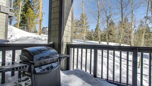 En grill på en balkong, med snö på marken och träd i bakgrunden.