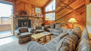 Una sala de estar acogedora con chimenea de piedra, techo de madera y ventanas amplias.