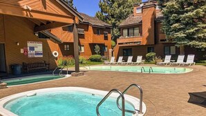 Zona de piscina con dos piscinas, sillas de descanso y un edificio de madera con un letrero de advertencia.