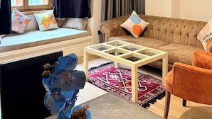 A living room with a sofa, a coffee table, a window with curtains, a hanging light fixture, and a small rug. - Taksim Square1br Suite 02 (Istanbul)