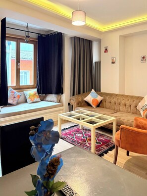 A living room with a sofa, a coffee table, a window with curtains, a hanging light fixture, and a small rug. - Taksim Square1br Suite 02 (Istanbul)