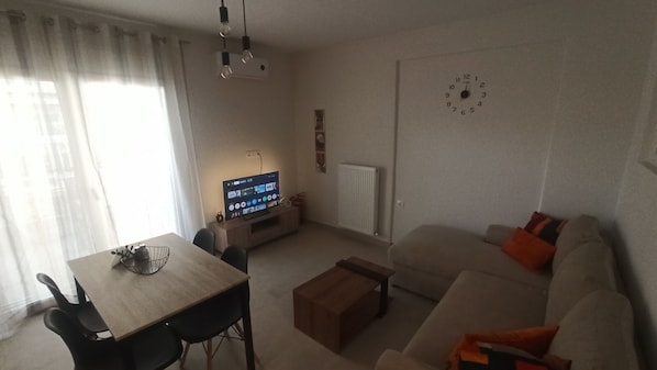 A living room with a sofa, a coffee table, a TV, and a dining area with chairs and a table.