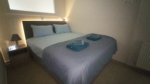 A hotel room with a bed, a nightstand, a lamp, and a window.