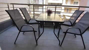 Un balcon avec une table et quatre chaises, une plante en pot sur la table, et une vue sur des bâtiments en arrière-plan.