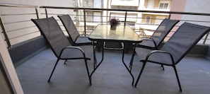 A balcony with a table and four chairs, a potted plant on the table, and a view of buildings in the background.