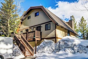 A two-story house with a wooden staircase leading to a balcony, surrounded by snow. - Spacious, updated townhouse with deck & sauna (Mammoth Lakes)