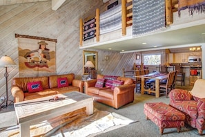 A cozy living room with a sofa, a coffee table, and a dining area with a table and chairs. - Creekside townhome with shared hot tub, deck offering panoramic views (Mammoth Lakes)