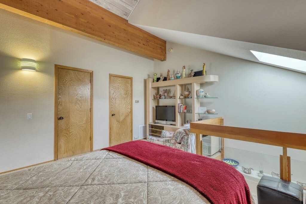 Ein Schlafzimmer mit einem Bett, Holzboden, einem Regal mit Dekoration und einem Fernseher.