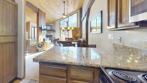 A kitchen with granite countertops, wooden cabinets, a stove, and a dining area with a chandelier. - Townhome Near Skiing with Fireplace & Shared Pool, Hot Tub Access, Dog-Friendly (Mammoth Lakes)