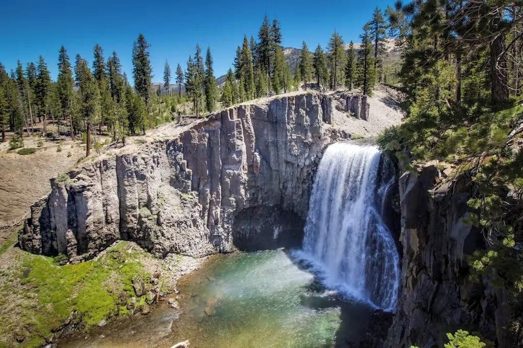 Un paisaje natural con cascada, riscos rocosos y árboles circundantes.