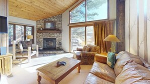 A cozy living room with a stone fireplace, leather sofa, and a wooden coffee table. - Townhome Near Skiing with Fireplace & Shared Pool, Hot Tub Access, Dog-Friendly (Mammoth Lakes)