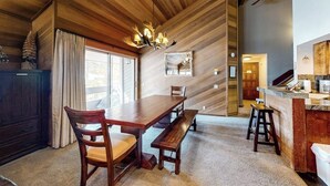Un intérieur en bois comprenant une table à manger, des chaises, un banc, un lustre et un coin cuisine.
