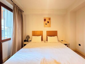 A hotel room with a large bed, two nightstands, a lamp, a window with curtains, and a wall art piece. - Taksim Square1 Bedroom Suite 03 (Istanbul)