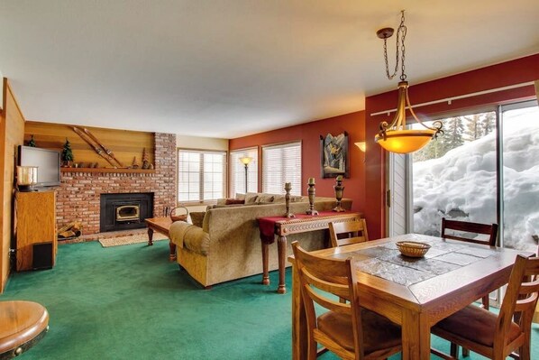 A cozy living room with a fireplace, a dining area, and a view of snow outside. - Updated Rental with Shared Hot Tub & Pool, Updated Kitchen (Mammoth Lakes)