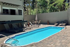A rectangular swimming pool with a tiled edge, surrounded by lounge chairs and a table with umbrellas. - Updated Rental with Shared Hot Tub & Pool, Updated Kitchen (Mammoth Lakes)