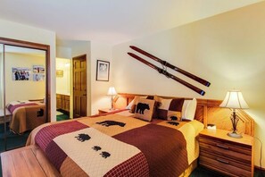 A hotel room with a large bed, a wooden headboard, a mirror, a picture on the wall, and a pair of skis hanging on the wall. - Updated Rental with Shared Hot Tub & Pool, Updated Kitchen (Mammoth Lakes)