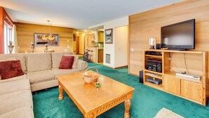 Uma sala de estar com sofá, mesa de centro de madeira, televisão e aparador de madeira com dispositivos eletrônicos.