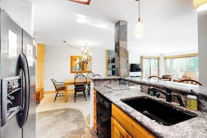 A kitchen with granite countertops, a stone pillar, a dining area with chairs, and a large window. - Condo with Shared Hot Tubs, Pool, and Sauna & Great Mountain Views (Mammoth Lakes)
