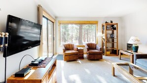 Ein Wohnzimmer mit Fernseher, Ledersesseln, Bücherregal und Blick auf Bäume.