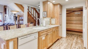 Une cuisine dotée de meubles en bois, d’un plan de travail en granit, d’un lave-vaisselle et d’un escalier menant à une mezzanine.