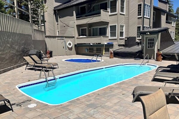 Una piscina rectangular con revestimiento azul, rodeada de sillones de descanso y un jacuzzi pequeño.