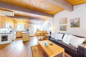 Eine moderne Küche mit Holzausstattung, ein Essbereich mit Tisch und Stühlen, ein Wohnzimmer mit Sofa und Couchtisch sowie Kunstwerke an den Wänden.