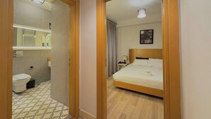 Quarto de hotel com cama de madeira, banheiro com vaso sanitário e pia, e um espelho.