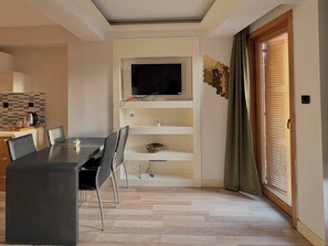 Ein modernes Wohnzimmer mit Essbereich, einem an der Wand befestigten Flachbildfernseher, einer Holztür und einer gefliesten Spritzschutzwand.