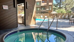 Ein Schwimmbecken mit Metallleiter, ein Schild mit Hinweis auf einen Not-Aus-Schalter für das Spa und Blick auf ein Gebäude mit einer Terrassenanlage.