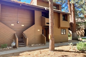 A modern multi-story building with a wooden exterior, a staircase, and a tree in the foreground. - Charming Ground-Level Condo with Shared Hot Tub, Pool, Sauna, & Tennis Courts (Mammoth Lakes)