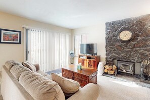 Ein Wohnzimmer mit einer Couch, einem Fernseher, einem Kamin und einer Steinwand.