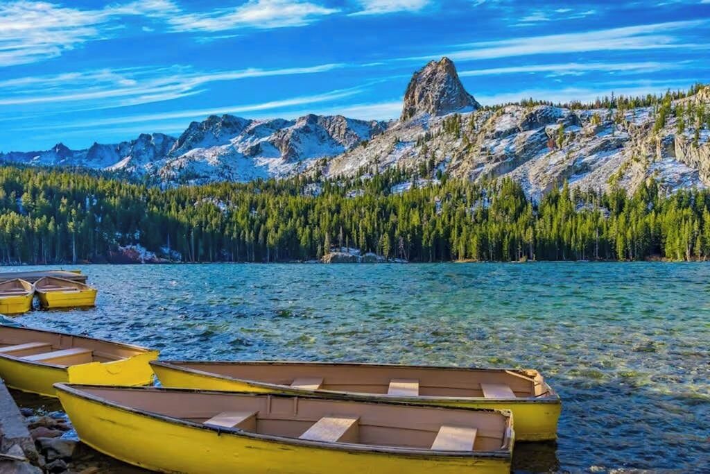 A lake with boats, clear water, and a mountain range in the background.