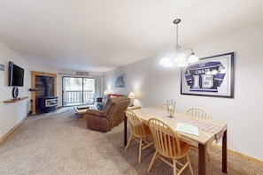 A cozy living room with a fireplace, a dining table with chairs, a sofa, and a framed picture on the wall. - Cozy Retreat with Patio, WiFi, Shared Pool, Hot Tub & Sauna - Near Slopes & Golf (Mammoth Lakes)