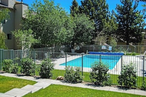 Ein rechteckiger Swimmingpool, umgeben von einem Metallzaun, mit blauem Himmel und Grün im Hintergrund.