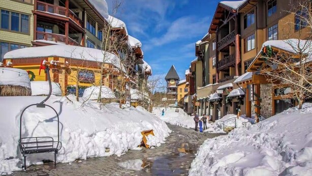 Una strada innevata con edifici, una seggiovia e un piccolo ruscello.
