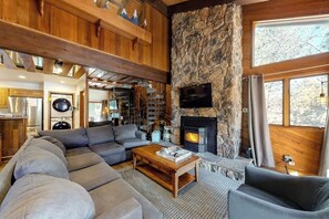 Ein gemütliches Wohnzimmer mit Kamin aus Stein, einer großen Couch und einem an der Wand befestigten Fernseher.