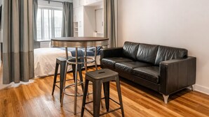 Un salon moderne avec un canapé en cuir, une table ronde avec des tabourets et un lit doté d’une tête de lit blanche.