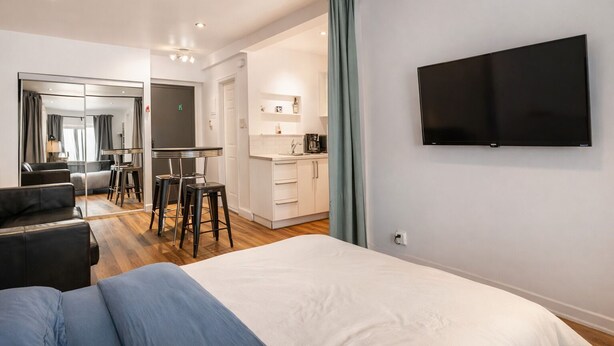 Une chambre d’hôtel moderne équipée d’un lit, d’une télévision, d’une kitchenette et d’un coin salon avec une table et des chaises.