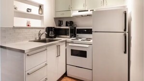 Une cuisine de taille réduite, avec des meubles blancs, une cuisinière, un four à micro-ondes et un réfrigérateur.