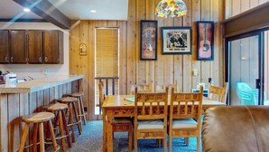 Un interior de madera con una mesa de comedor, taburetes de bar y cuadros en la pared.