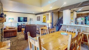 Amplia sala de estar con una mesa de comedor de madera, sofás de cuero, un televisor y una zona de cocina con refrigerador.