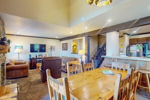 A spacious living area with a wooden dining table, leather sofas, a TV, and a kitchen area with a refrigerator. - Skier's paradise with mountain views, pool, hot tub & game room - dog-friendly (Mammoth Lakes)