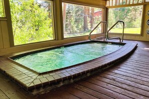 A hot tub with a tiled edge, wooden deck, and large windows with a forest view. - Skier's paradise with mountain views, pool, hot tub & game room - dog-friendly (Mammoth Lakes)