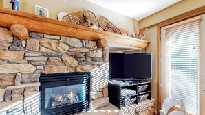 A stone fireplace with a TV, a wooden shelf above it, and a white chair to the right. - Convenient mountain getaway with views & on-site golf - near skiing (Mammoth Lakes)