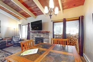 A living room with a stone fireplace, a television, a dining table, and a fireplace mantel. - Modern condo with WiFi, fireplace, pool, & hot tub - near local attractions (Mammoth Lakes)